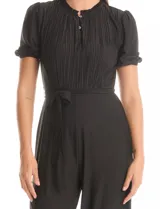 Enterito largo negro de seda fría, marca Sharagano. Presenta cuello a la base con frunces y escote en V con botones metálicos. La parte delantera tiene un detalle plisado vertical. Mangas cortas con terminación fruncida. Incluye un lazo de ajuste en la cintura y pantalón de pierna ancha y largo total. La espalda cuenta con cierre oculto.