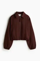 Campera oversized de sarga color marrón, con cuello, cierre frontal y bolsillos laterales ribeteados. Cuenta con mangas abullonadas, puños elásticos y bajo globo para una silueta redondeada.