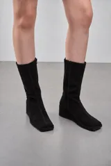 Bota de caña alta confeccionada en gamuza color marrón, con punta cuadrada, taco cuña corrido forrado y cierre lateral.