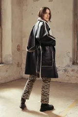 Cazadora larga de estilo doble faz, confeccionada en cuero sintético negro con interior de corderito sintético color crema. Presenta un diseño de corte recto, cierre frontal con botones, solapas amplias y bolsillos laterales.