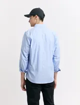 Camisa de corte clásico confeccionada en tejido oxford, con diseño de rayas verticales en tonos azul y blanco. Presenta cuello abotonado, cierre frontal con botones y bolsillo en el pecho con detalle de etiqueta bordada.