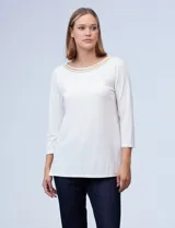 Blusa blanca de tejido elastizado marca Ruby Rd. Tiene escote redondo con aplique metálico y mangas 3/4.