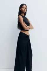 Pantalón de tiro alto negro, de corte holgado y pernera recta, confeccionado en punto grueso. Presenta un diseño drapeado con un detalle de nudo o giro en la parte frontal de la cintura.