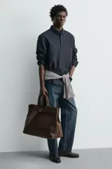Bolso de mano de piel marrón oscuro de alta calidad con detalle de cinturón decorativo con hebilla metálica dorada y dos asas cortas.