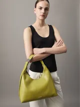 Cartera tipo hobo de piel sintética color verde lima, con cierre de cremallera superior y correa de hombro ajustable con herraje metálico. Presenta el logo de Calvin Klein grabado en la parte frontal inferior.