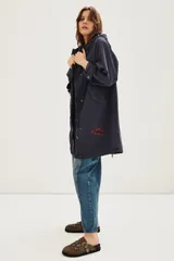 Campera tipo parka de canvas color azul marino, con capucha, cierre frontal y bolsillos laterales. Presenta un bordado en hilo rojo en la parte inferior frontal con la frase 'She's Electric'.