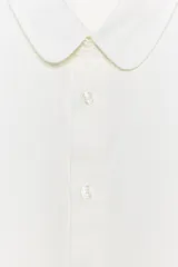 Camisa blanca de manga larga con cuello redondo tipo bebé y cierre frontal de botonadura simple.