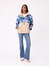 Canguro de estilo deportivo con diseño combinado, parte superior con estampado floral en tonos azules y rosados, y parte inferior de tejido tipo sherpa en color beige. Cuenta con cuello alto, cierre frontal parcial y bolsillo tipo canguro frontal con logo de la marca.