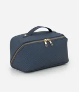 Neceser tipo baúl de color azul marino con textura trenzada. Cuenta con asa superior fija, cierre metálico doble en color dorado y estructura rígida.