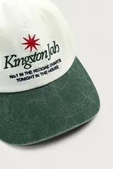 Gorra de seis paneles con efecto lavado, de color blanco crudo con visera en verde militar. Presenta un bordado frontal contrastante con texto en negro y una estrella roja.