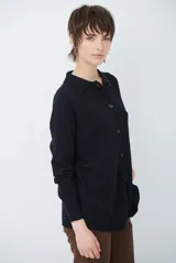 Cardigan de punto color beige, con cuello camisero, cierre frontal de botones y bolsillo aplicado en el pecho. Presenta mangas largas con puños acanalados y un corte recto y holgado.