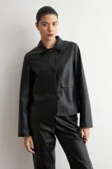 Chaqueta de eco cuero negro con cuello camisero, cierre frontal oculto y mangas largas con puños rectos.
