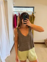 Blusa de tejido de punto con acabado brillante, escote en V profundo y espalda abierta. Presenta un diseño holgado y sin mangas.