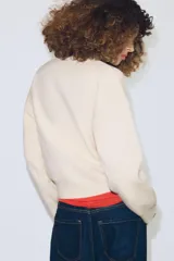 Jersey de punto con cuello tipo polo, manga larga con puños y cierre frontal con botones. Presenta un bolsillo de plastrón en el pecho y diseño de corte holgado.