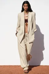 Blazer color beige confeccionada en lino, de corte recto, con cuello solapa, hombreras y mangas 3/4 con trabilla y botón dorado.