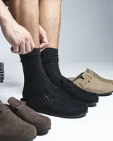 Zuecos cerrados al frente color negro, confeccionados en material símil gamuza. Presentan una tira ajustable con hebilla metálica en el empeine y una suela con detalle de corcho en el talón.