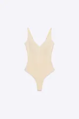 Body color beige claro, de tejido liso, con escote en pico pronunciado y tirantes anchos ajustables. Presenta cierre inferior con botones a presión.