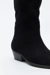 Bota texana de caña alta confeccionada en gamuza negra, con diseño de estilo western, costuras decorativas, tirador superior y taco bajo levemente inclinado.