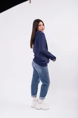 Canguro con capucha de color azul marino, confeccionado en tela deportiva con frizza. Presenta un diseño de calce holgado, mangas largas y puños elásticos.