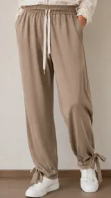 Pantalón de viscosa y algodón color beige, de corte relajado y estilo aladino, con cintura elastizada ajustable mediante cordón y lazos en los tobillos.