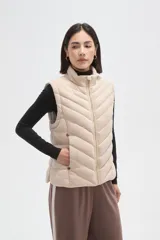 Chaleco acolchado de diseño capitoneado con cierre frontal y bolsillos laterales. Presenta un cuello alto y detalles de botones metálicos decorativos.