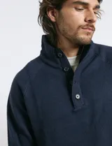 Sweater de punto color azul marino, con cuello alto, cierre frontal parcial y tapeta con botones. Presenta mangas raglán y puños y ruedo acanalados.