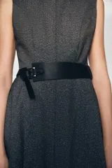 Vestido midi de cuello redondo y sin mangas, confeccionado en tejido jaspeado gris. Presenta un corte evasé y un cinturón ancho de cuero sintético negro con hebilla metálica. Incluye cierre posterior con cremallera oculta.