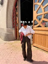 Camisa blanca de corte holgado y diseño amplio, con cuello clásico, mangas largas y un bolsillo frontal en el pecho adornado con un bordado rojo.