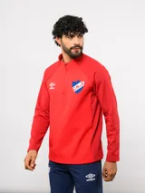 Buzo de entrenamiento Umbro del Club Nacional de Football, con medio cierre frontal, cuello alto y mangas largas. Presenta el logo de la marca y el escudo del club en el pecho.