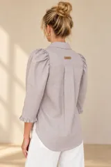 Camisa de lino color blanca, con cuello clásico, mangas tres cuartos abullonadas en los hombros y terminación con volados en los puños, cierre frontal con botones ocultos.
