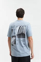 Remera de manga corta color celeste, con estampado gráfico en la espalda que incluye imágenes arquitectónicas en blanco y negro y texto.