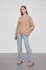 Sweater de tejido de punto en color beige, con cuello en V cruzado y mangas largas con puños ajustados.