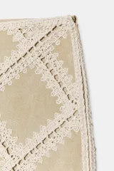 Minifalda de tiro medio confeccionada en ante color beige, decorada con aplicaciones de tejido tipo crochet blanco formando un patrón de rombos. Cuenta con cierre de cremallera oculta en la costura.