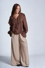 Blusa de color marrón con escote en V, mangas largas abullonadas con puños elásticos y detalles de volados en los hombros y el frente.