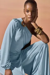 Body de un solo hombro confeccionado en jersey elástico. Presenta un diseño drapeado con una hebilla decorativa dorada en el hombro, manga larga con puño y detalle de fruncido en la cintura.