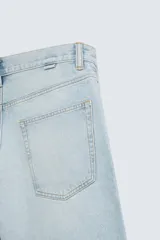 Bermuda de denim de algodón, color azul medio lavado, de corte ancho (baggy fit) y largo hasta la rodilla. Presenta cinco bolsillos y cierre frontal con cremallera y botón.