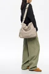 Bolso shopper de nylon color negro, con estructura blanda, doble asa de mano y correa ajustable extraíble. Presenta bolsillos laterales con cierre y logo metálico de la marca en la parte inferior.