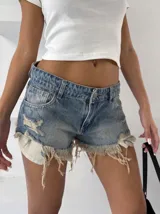 Short de denim azul con efecto desgastado, roturas extremas y flecos en los laterales.