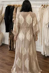 Kaftan largo de tejido translúcido color tostado con estampado metalizado dorado en forma de hojas, mangas amplias y cordón ajustable en la cintura.