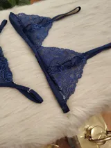 Conjunto de lencería de encaje en color azul profundo, compuesto por un corpiño triangular sin aro y una bombacha tipo colaless con detalles de encaje y transparencias.