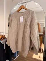 Sweater de tejido de punto grueso con diseño de trenzas en relieve, cuello redondo, mangas largas y terminaciones acanaladas en puños, cuello y cintura.