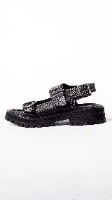 Sandalias negras de cuero con suela track gruesa. Presentan dos tiras ajustables con hebillas metálicas cuadradas en la parte superior del pie y una tira de ajuste en el talón.