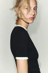 Camiseta blanca de manga corta y cuello redondo, con ribete negro decorado con perlas blancas en el cuello y los puños.