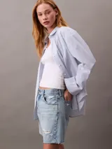 Short de jean de tiro alto con diseño de cinco bolsillos, cierre de cremallera y botón, con detalles de roturas y ruedo deshilachado.