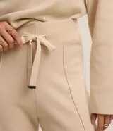 Pantalón wide leg de punto color beige, de tiro medio con cintura elástica ancha de rib, lazo ajustable con punteras metalizadas y costuras verticales decorativas.
