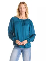 Blusa de satén color verde azulado con acabado sedoso y fluido. Escote a la base con frunce perimetral, mangas largas estilo balloon con detalle de punto smock en hombros y puños. Espalda con abertura tipo gota y botón forrado a tono.