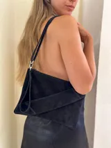 Cartera tipo sobre de cuero gamuza color negro, con solapa frontal y cierre de cremallera. Incluye una correa larga desmontable para usar al hombro o como bandolera, y una correa corta desmontable para la muñeca.