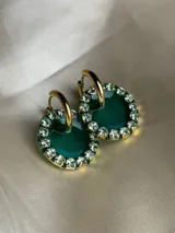 Aros colgantes dorados con dije circular de resina color turquesa, bordeado con strass. El arito es de acero quirúrgico.