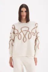 Conjunto de dos piezas compuesto por sweater de cuello redondo y pantalón de corte recto, ambos en color crema con diseño de arabescos bordados en tono beige.