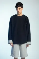 Buzo de felpa negro de corte oversize, con cuello redondo y mangas largas con puños grises doblados hacia afuera. Presenta costuras externas decorativas en tono gris claro a lo largo de las mangas y los hombros.